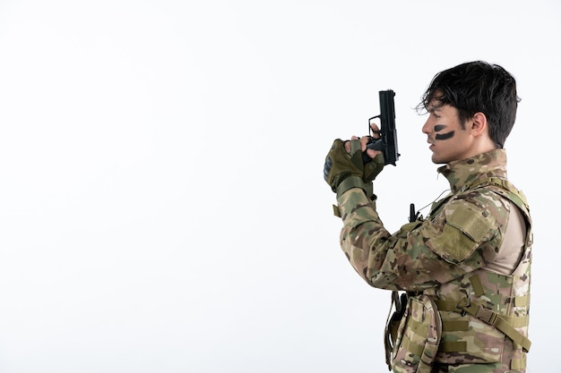 Portrait of young soldier in camouflage with gun studio shot white wall