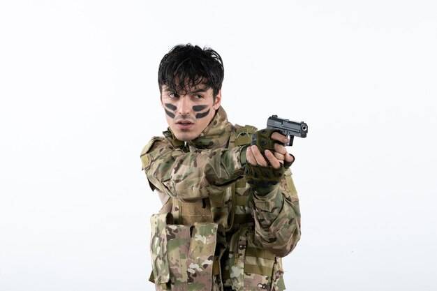 Portrait of young soldier in camouflage with gun on a white wall