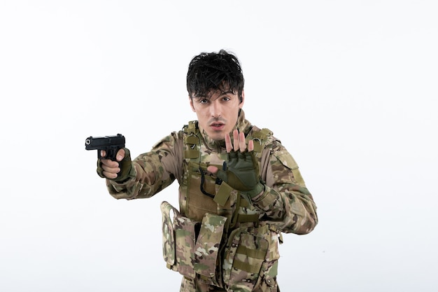 Portrait of young soldier in camouflage with gun on white wall