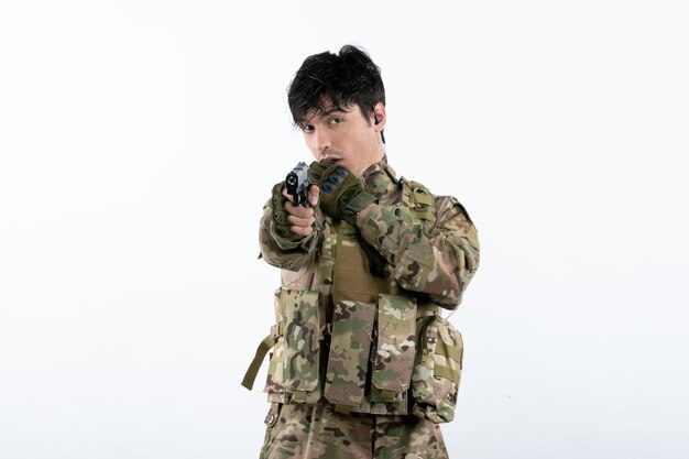 Portrait of young soldier in camouflage with gun on white wall