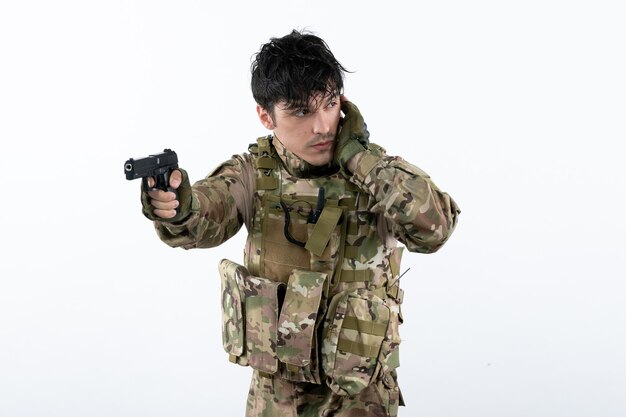 Portrait of young soldier in camouflage with gun on white wall