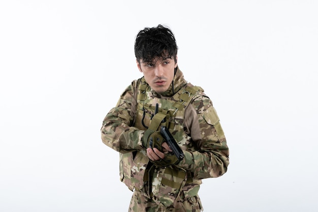 Portrait of young soldier in camouflage with gun on white wall