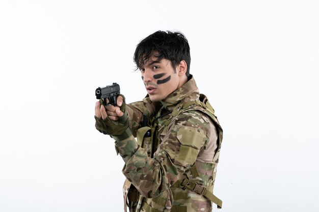 Portrait of young soldier in camouflage with gun on white wall