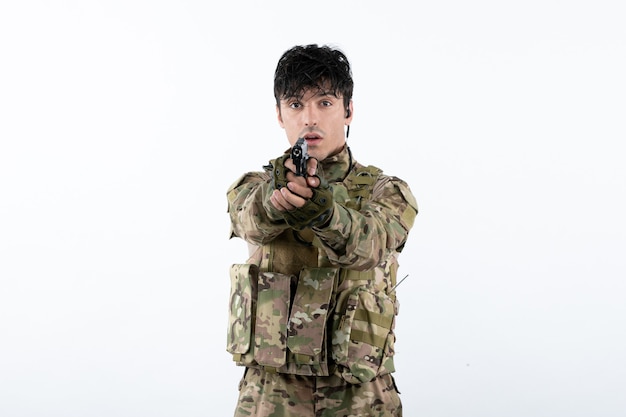 Портрет молодого солдата в камуфляже с пистолетом на белой стене