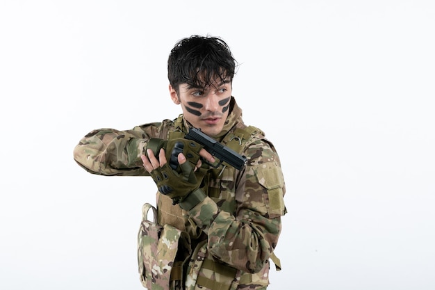 Portrait of young soldier in camouflage with gun on white wall