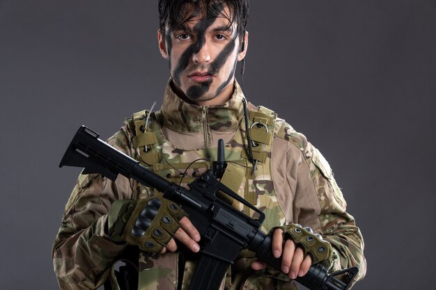 Portrait of young soldier in camouflage with machine gun on dark wall