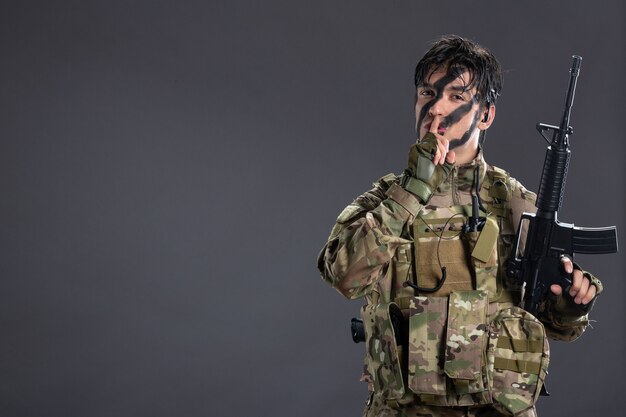 カモフラージュの暗い壁に機関銃を持つ若い兵士の肖像画