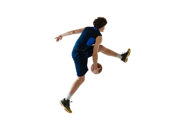 白いスタジオの背景に分離されたトレーニングバスケットボールをしている若いスポーツ少年の肖像画側面図