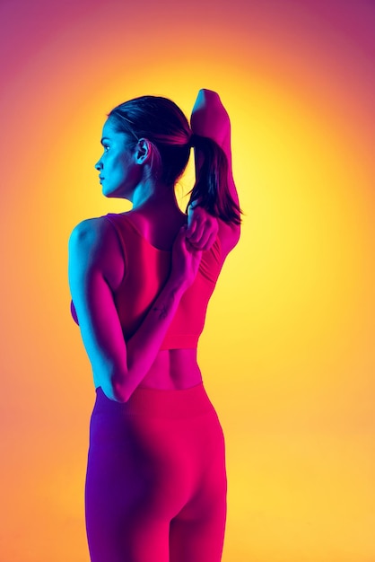 ネオンの色とりどりの背景に分離されたヨガとストレッチ運動をしている若いスポーツ女性の肖像画