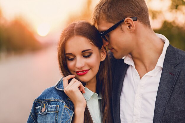 Portrait of young stylish fashion couple posing in summer sunset . Pretty young girl in jeans jacket and her handsome boyfriend walking .