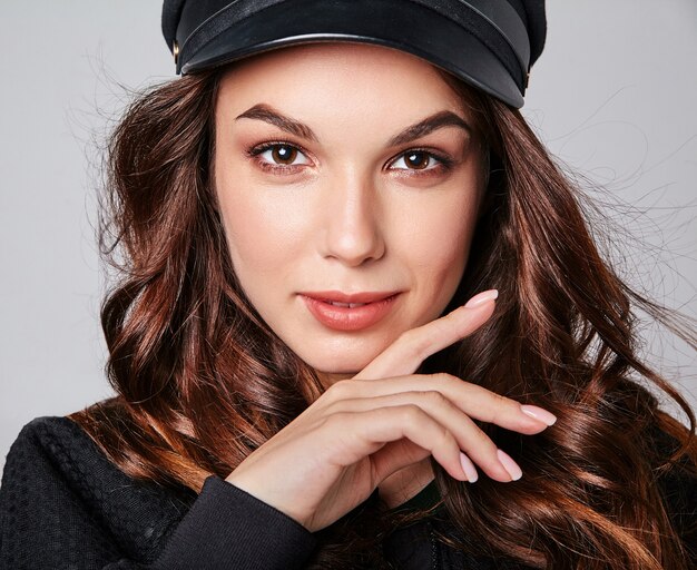 Portrait of young stylish laughing model in black casual summer clothes in cap with natural makeup on gray
