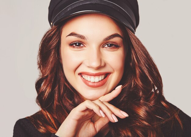 Portrait of young stylish laughing model in black casual summer clothes in cap with natural makeup on gray