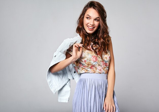 Портрет молодой стильной смеющейся модели в разноцветной повседневной летней одежде с естественным макияжем на сером