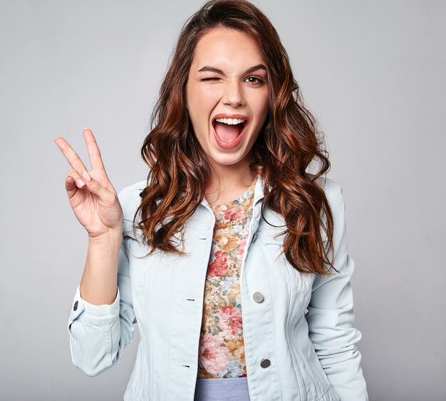 Portrait of young stylish laughing model in colorful casual summer clothes with natural makeup on gray