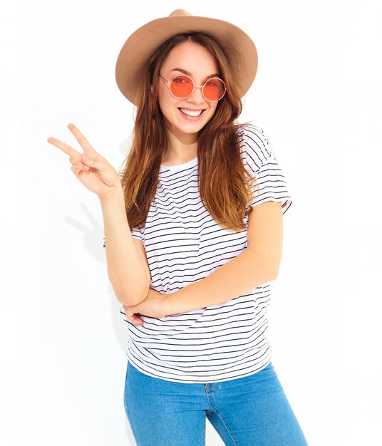 Portrait of young stylish laughing woman model in casual summer clothes in brown hat with natural makeup isolated on white wall. Showing peace sign