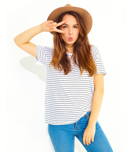 Portrait of young stylish laughing woman model in casual summer clothes in brown hat with natural makeup isolated on white wall. Showing peace sign