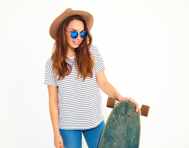 Longboard 책상 포즈 갈색 모자에 캐주얼 여름 옷에 세련 된 젊은 여자 모델의 초상화. 흰색에 고립
