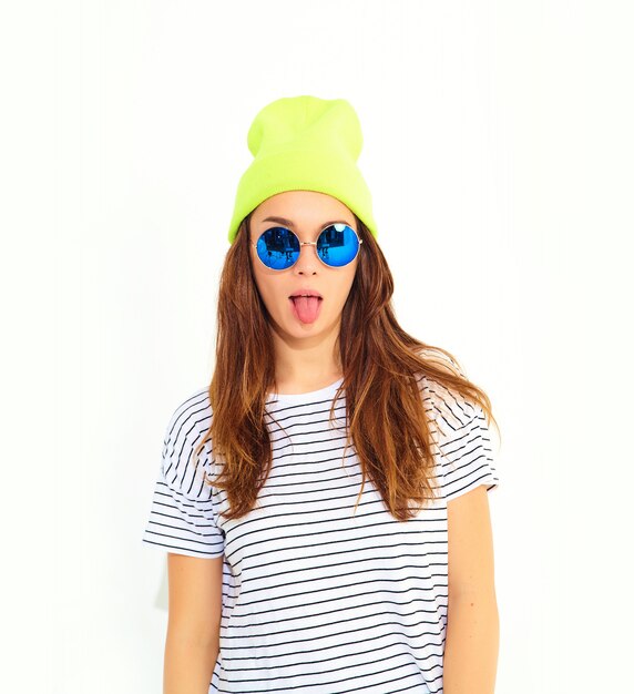 Portrait of young stylish woman model in casual summer clothes in yellow beanie hat isolated on white. Showing her tongue