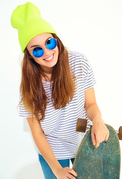 Foto gratuita il ritratto di giovane modello alla moda della donna in estate casuale copre in cappello giallo del beanie che posa con lo scrittorio di longboard. isolato su bianco