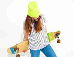 Foto gratuita il ritratto di giovane modello alla moda della donna in estate casuale copre in cappello giallo del beanie che posa con lo scrittorio di longboard. isolato su bianco