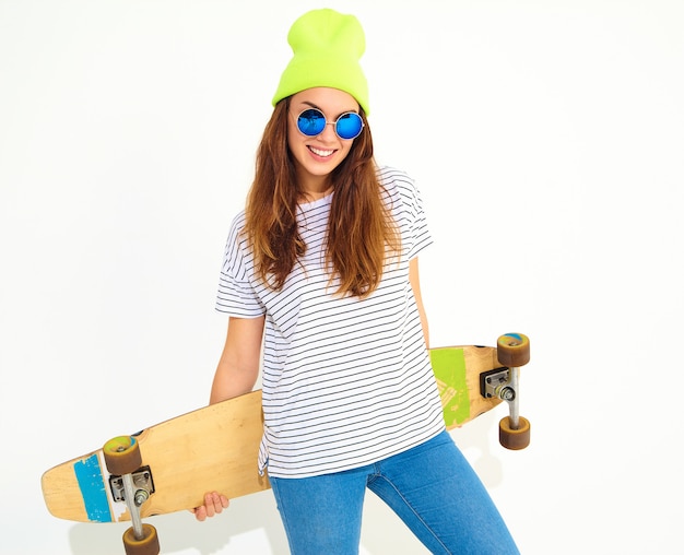 Free photo portrait of young stylish woman model in casual summer clothes in yellow beanie hat posing with longboard desk. isolated on white