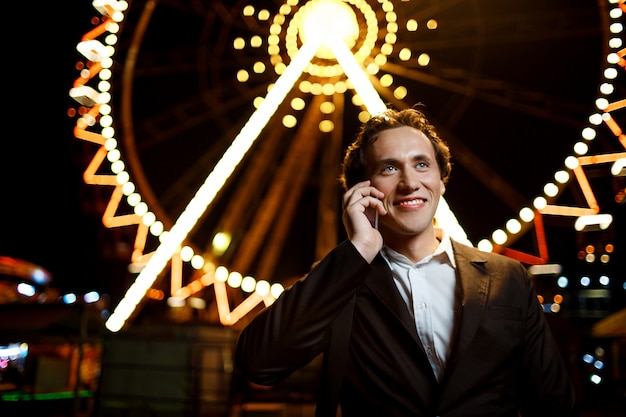 Portrait of young successful businessman over night amusement park. shallow dof