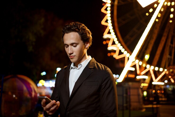 Portrait of young successful businessman over night amusement park. Shallow DOF