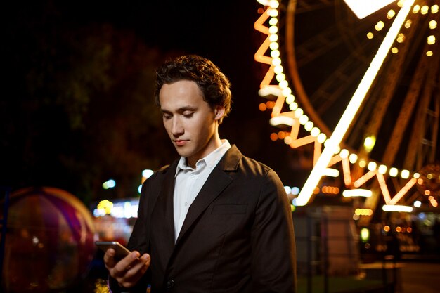 Portrait of young successful businessman over night amusement park. Shallow DOF