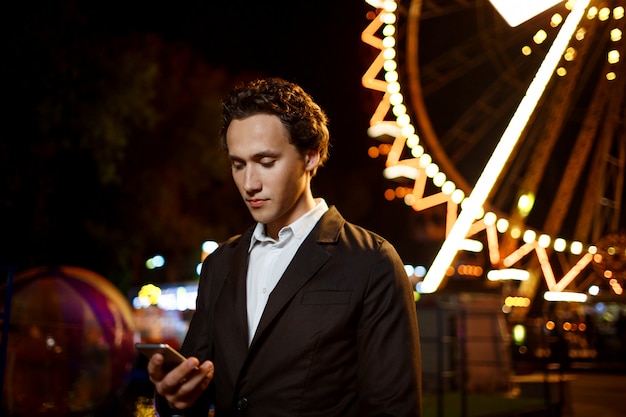 Портрет молодого успешного бизнесмена над парком развлечений ночи. Неглубоко ФО
