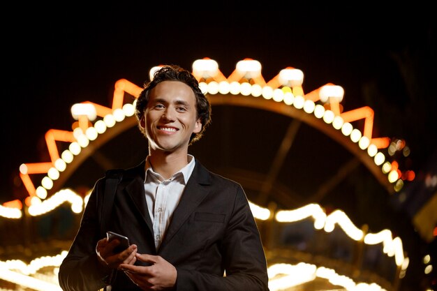 Portrait of young successful businessman over night amusement park. Shallow DOF