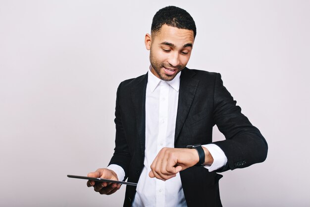 Portrait young successful  busy man in white shirt, black jacket, with tablet looking at watch. Stylish businessman, being busy, time for work, meeting, leadership.