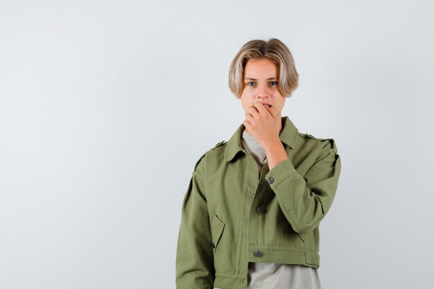 Portrait of young teen boy keeping hand on mouth in t-shirt, jacket and looking anxious front view