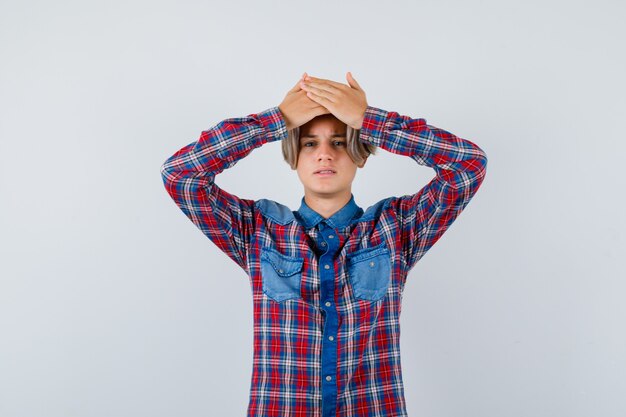 Portrait of young teen boy keeping hands on head in checked shirt and looking forgetful front view