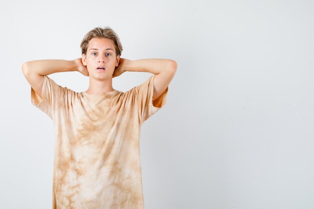 Portrait of young teen boy keeping hands behind head in t-shirt and looking bewildered front view