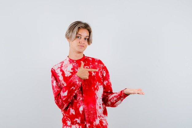 Portrait of young teen boy pointing at his palm spread aside in shirt and looking confident front view