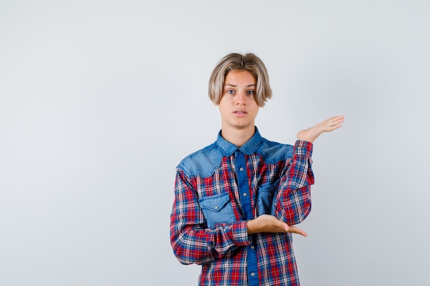 Portrait of young teen boy pretending to hold something in checked shirt and looking puzzled front view