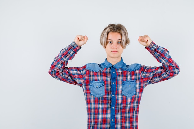 Foto gratuita ritratto di giovane ragazzo adolescente che mostra i muscoli delle braccia in camicia a quadri e guardando fiducioso vista frontale