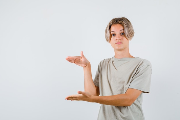 Free photo portrait of young teen boy showing size sign in t-shirt and looking puzzled front view