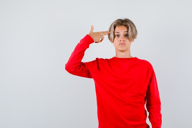 Portrait of young teen boy showing suicide gesture in red sweater and looking puzzled front view