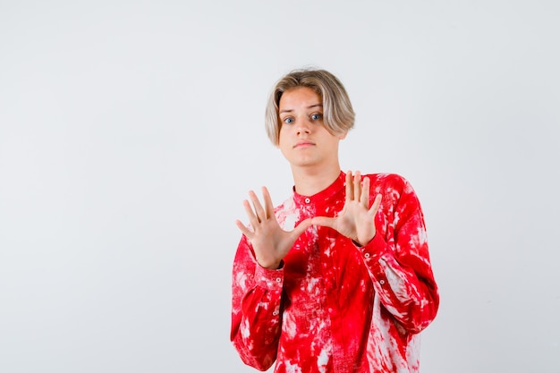 Portrait of young teen boy showing surrender gesture in shirt and looking frightened front view