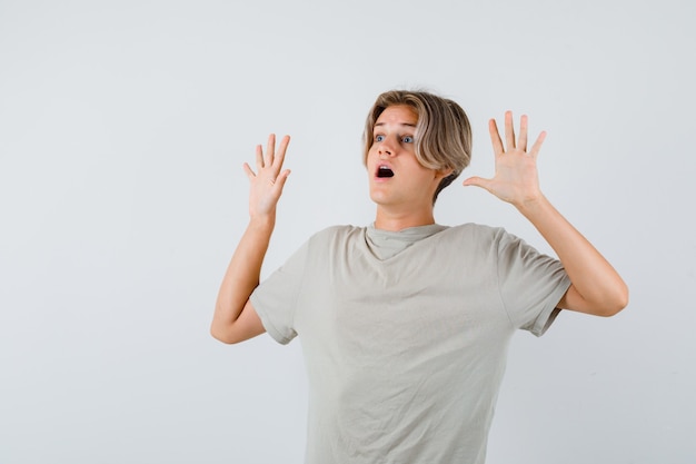 Portrait of young teen boy showing surrender gesture in t-shirt and looking scared front view