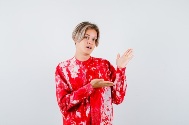 Portrait of young teen boy showing welcoming gesture in shirt and looking confident front view