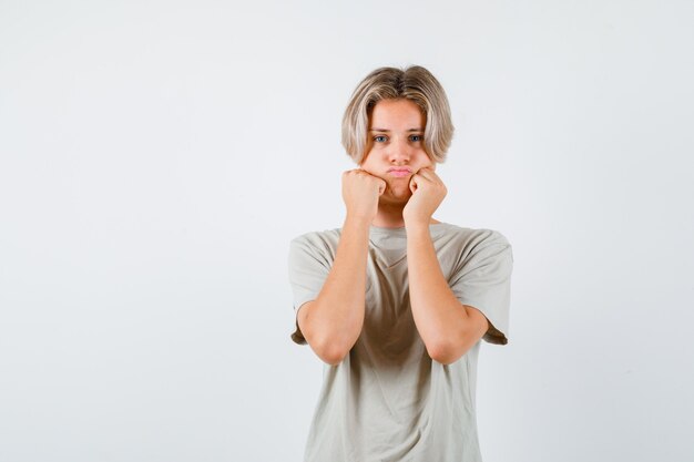 Portrait of young teen boy sulking with puffy cheeks leaning on hands in t-shirt and looking disappointed front view