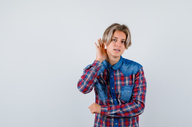 Portrait of young teen boy with hand behind ear in checked shirt and looking confused front view