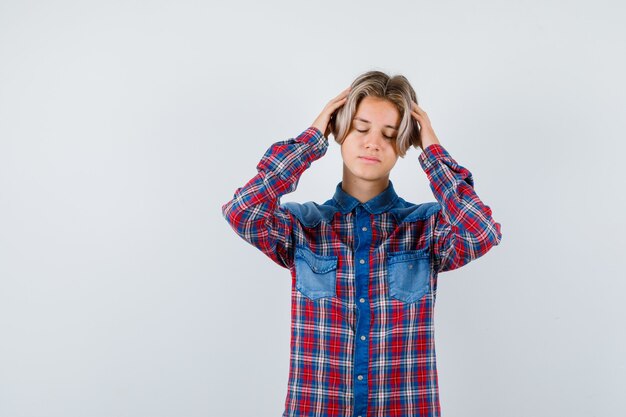 Portrait of young teen boy with hands on head in checked shirt and looking exhausted front view