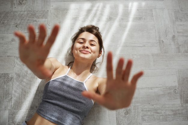 Portrait of young tender beautiful woman smiling stretching hands lying on floor in morning sunlights.