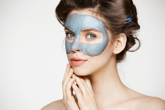 Portrait of young tender woman in hair curlers and facial mask smiling. Beauty and skincare concept.