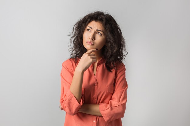 Portrait of young thoughtful brunette woman in orange shirt