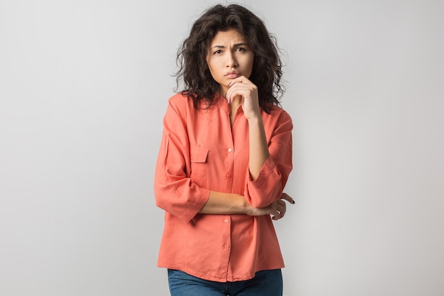 Portrait of young thoughtful brunette woman in orange shirt