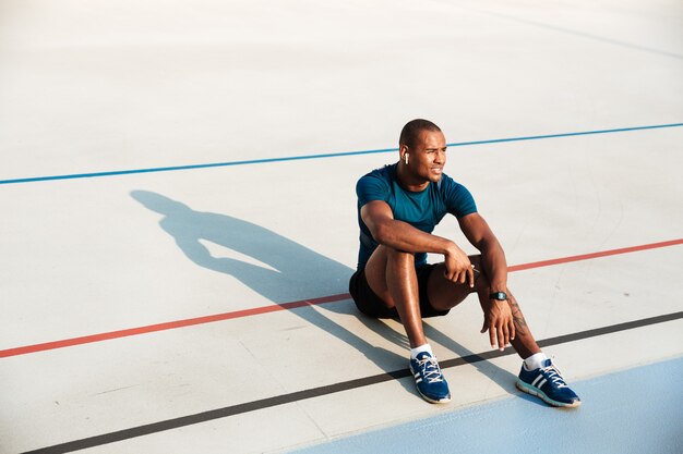 Portrait of a young tired african fitness man in earphones resting